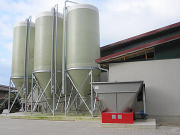 Ein Silo aus glasfaserverstärktem Kunststoff (GFK) von IBO Stalltechnik. Dieses Silo ist Teil eines automatischen Trockenfütterungssystems, das speziell für die Lagerung und Zuführung von CCM (Corn Cob Mix) oder anderem Trockenfutter in Schweineställen eingesetzt wird. Das Bild zeigt das Silo, typischerweise im Außenbereich einer Stallanlage installiert.